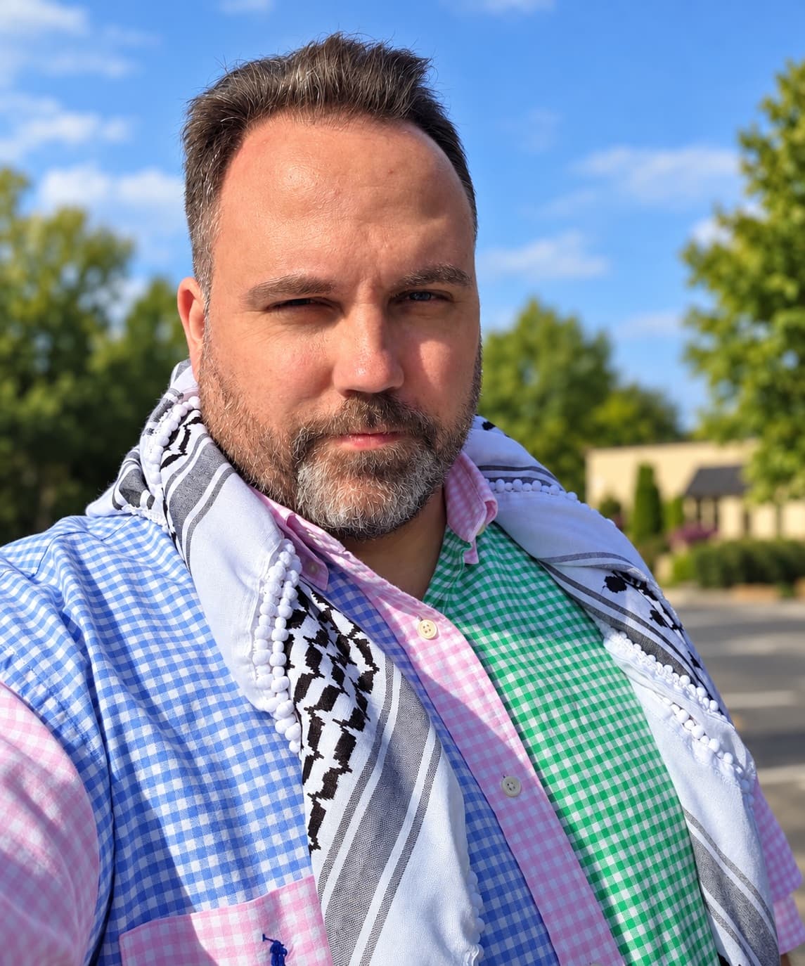 Ryan Michael Kelly outdoors wearing a black-and-white Palestinian keffiyeh.