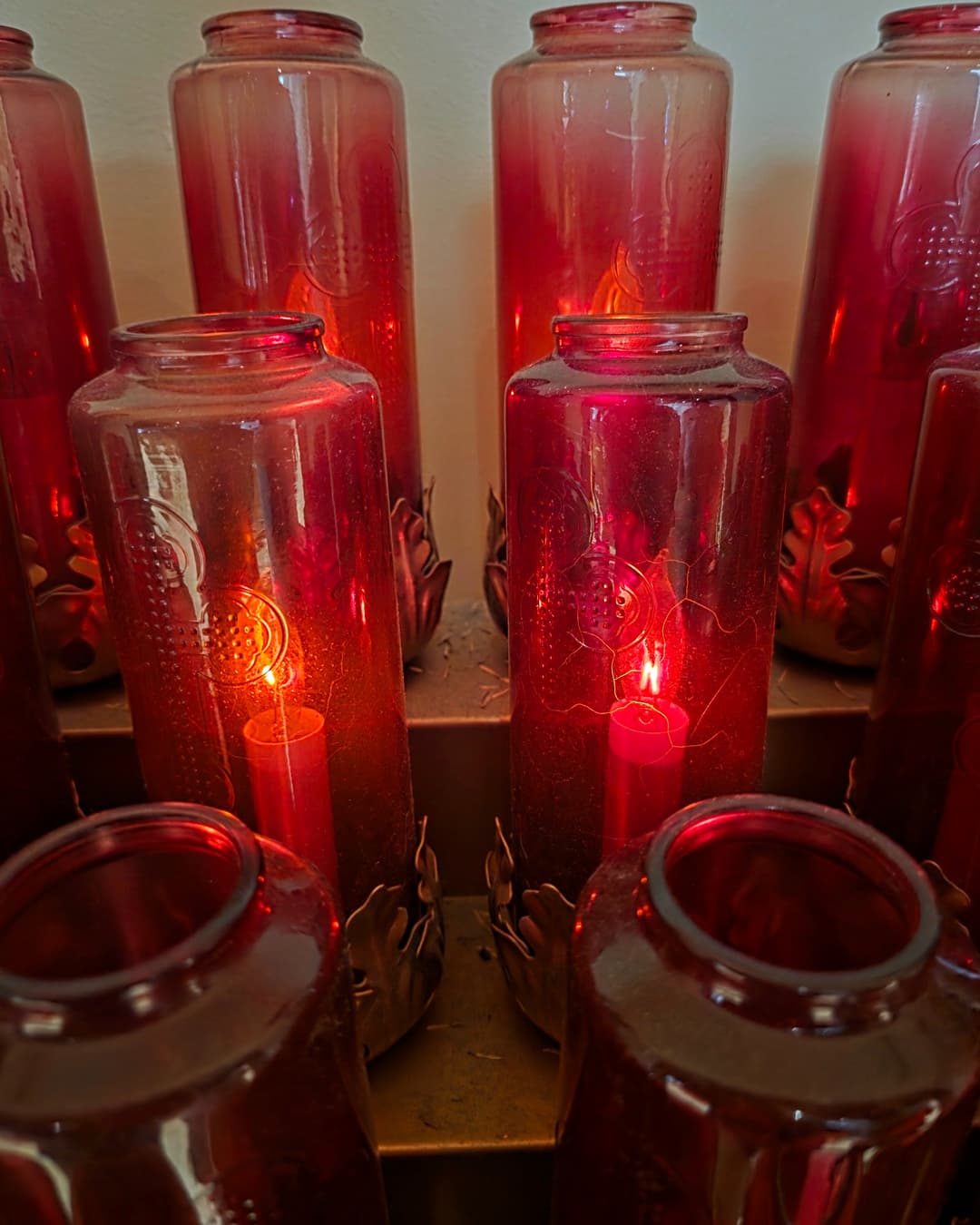 Two red votive candles burning side by side among other candles at a church, lit in memory of Alok Mehta and Fred Morrone