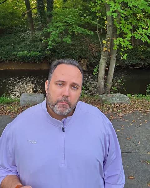 Ryan Michael Kelly speaking outdoors beside a wooded stream in his NJ-03 forum response video