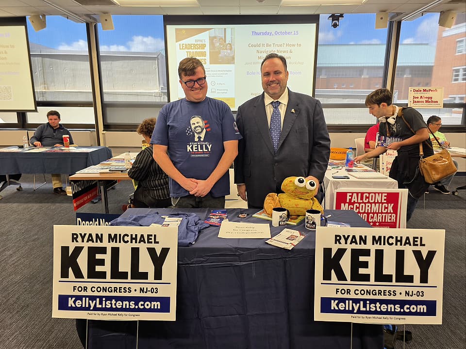 Ryan Michael Kelly y el estudiante voluntario de Rowan, Ian, están detrás de la mesa de Kelly for Congress en la Feria de Voluntariado de Campañas Políticas de RIPPAC en Rowan University